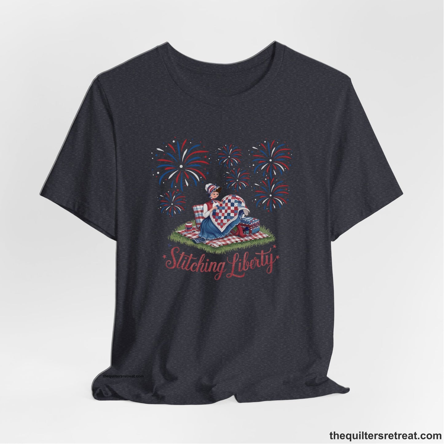 A Heather Navy Short Sleeve T-Shirt with a vintage illustration of woman quilting with fireworks and "Stitching Liberty" text in patriotic style
