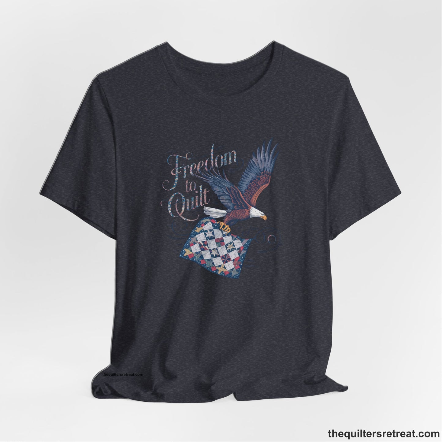 A Heather Navy Short Sleeve T-Shirt with a freedom to quilt text with an eagle carrying a colorful patchwork quilt in vintage style