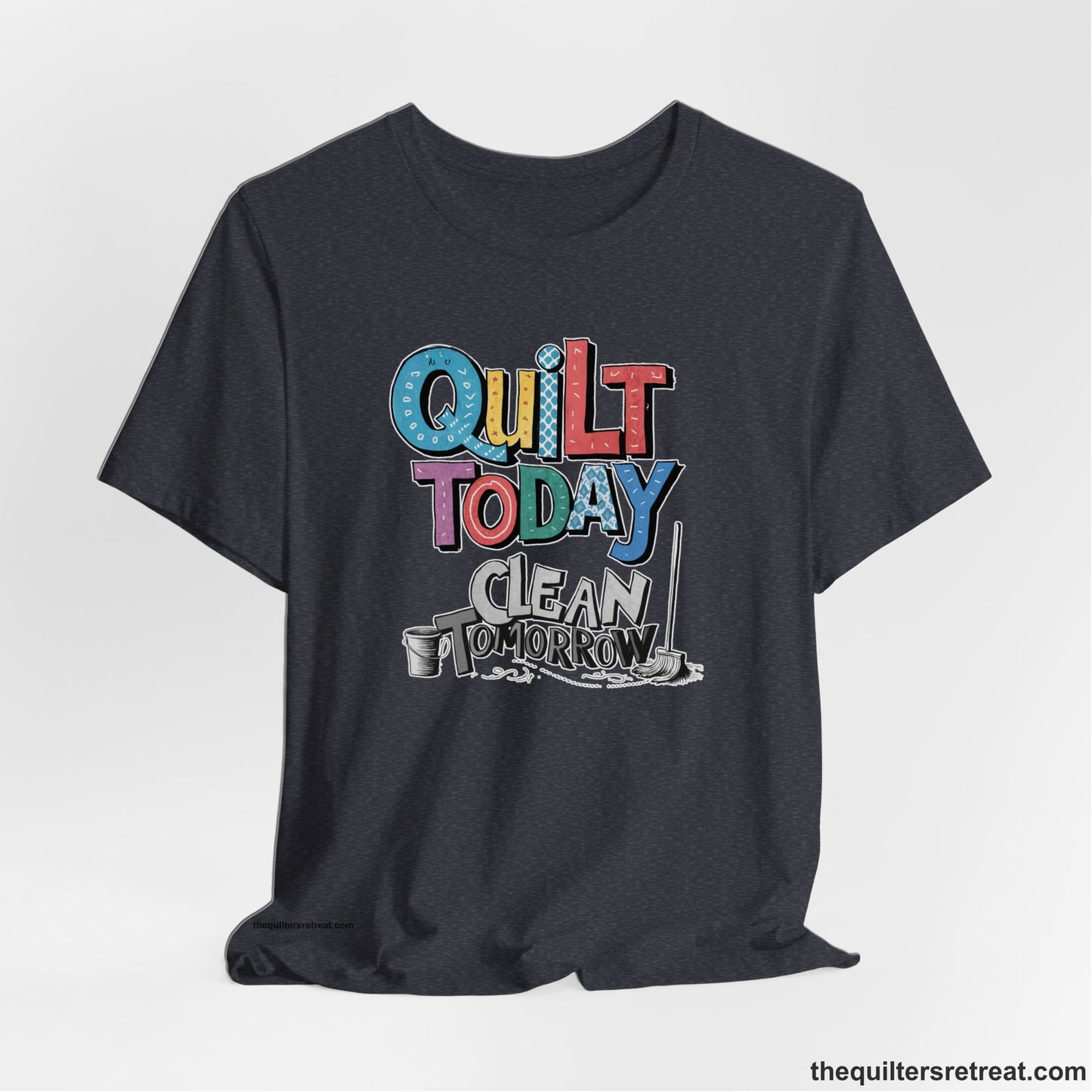 A Heather Navy Short Sleeve T-Shirt with a playful "Quilt Today Clean Tomorrow" text with colorful patterns and cleaning tools illustration