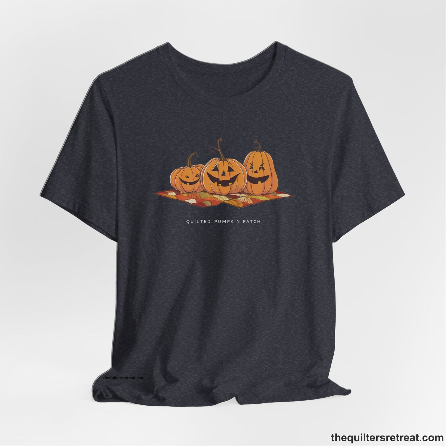 A Heather Navy Short Sleeve T-Shirt with a playful jack-o'-lantern trio on a quilt with "Quilted Pumpkin Patch" text