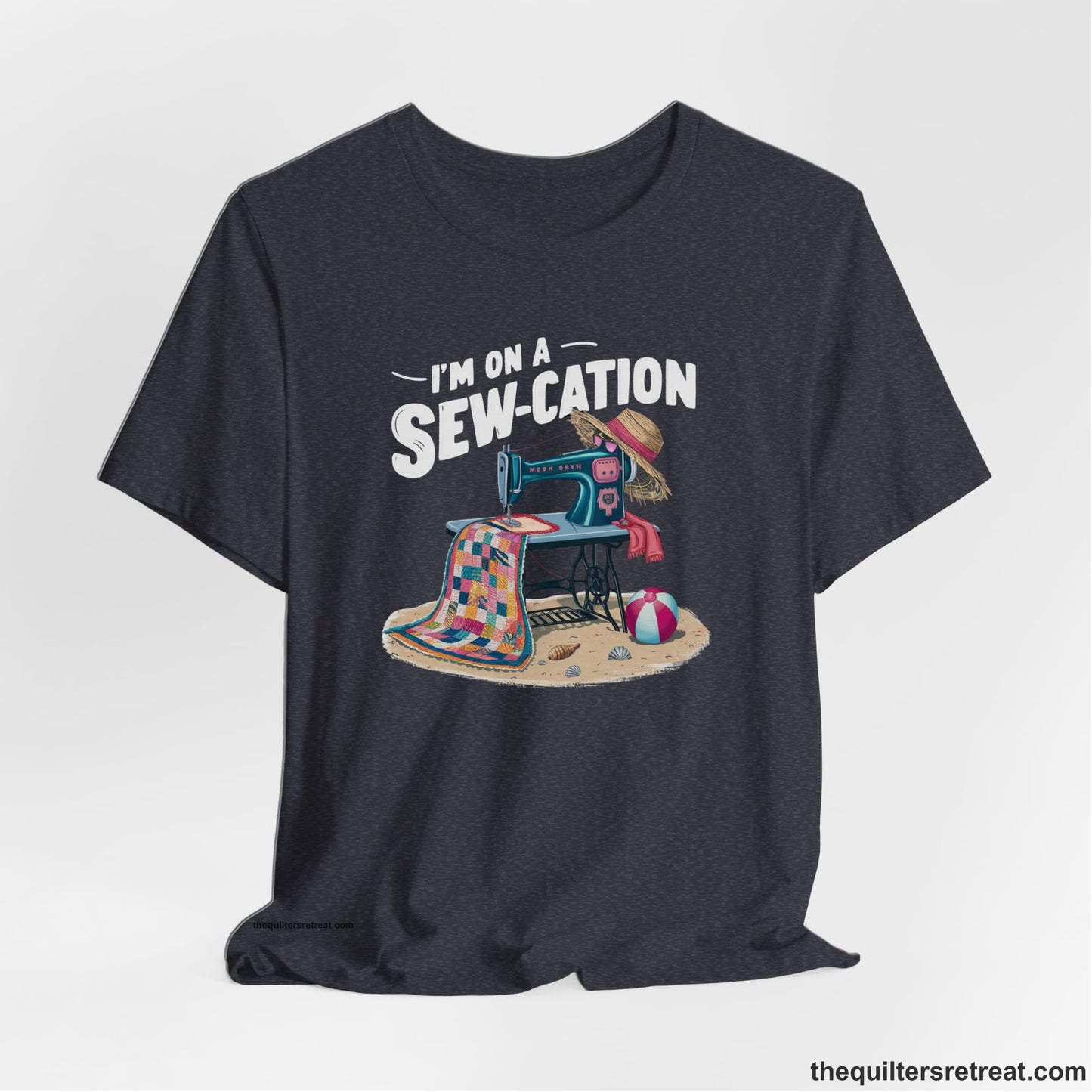 A Heather Navy Short Sleeve T-Shirt with a vintage sewing machine with colorful quilt, beach items, and "I'm On A Sew-Cation" text