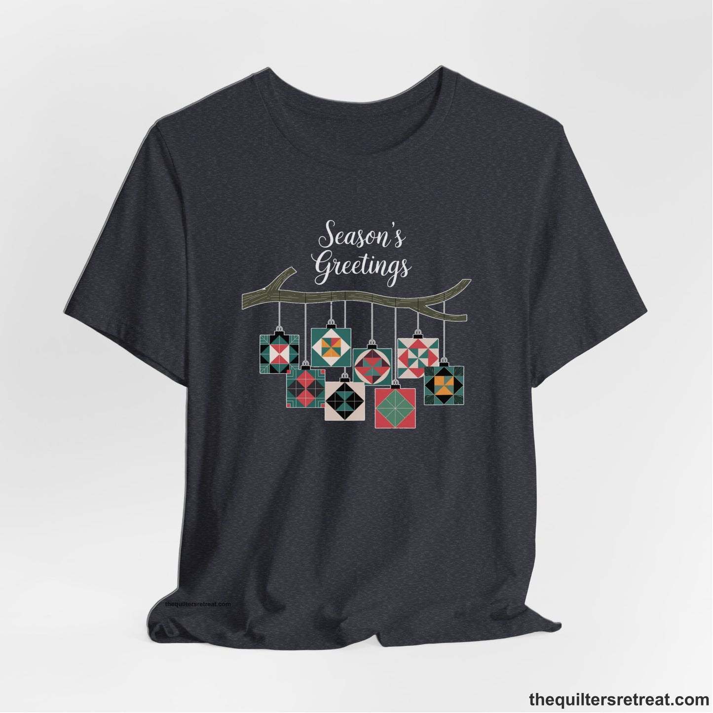 A Heather Navy Short Sleeve T-Shirt with a season's greetings text above colorful quilt block ornaments on tree branch in rustic style