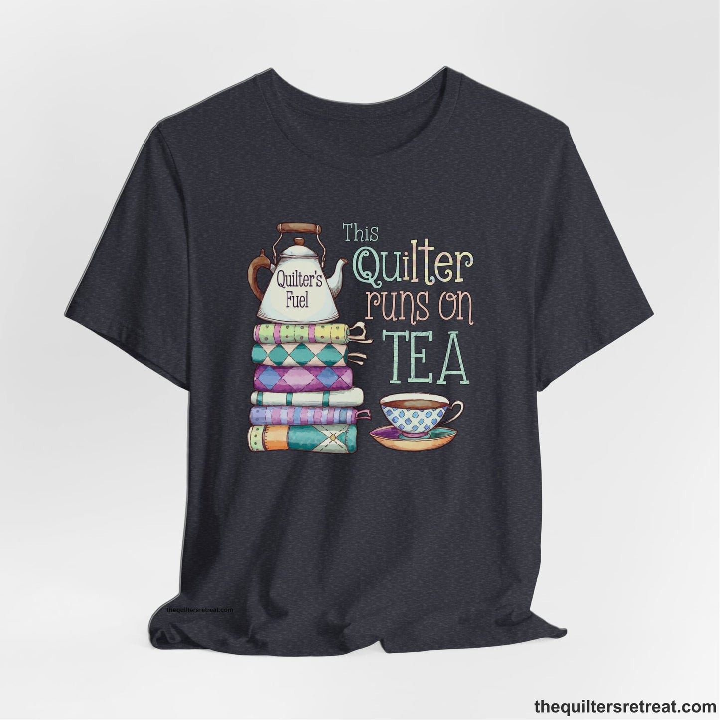 A Heather Navy Short Sleeve T-Shirt with a stack of colorful quilts with teapot and cup, whimsical "This Quilter Runs on Tea" text