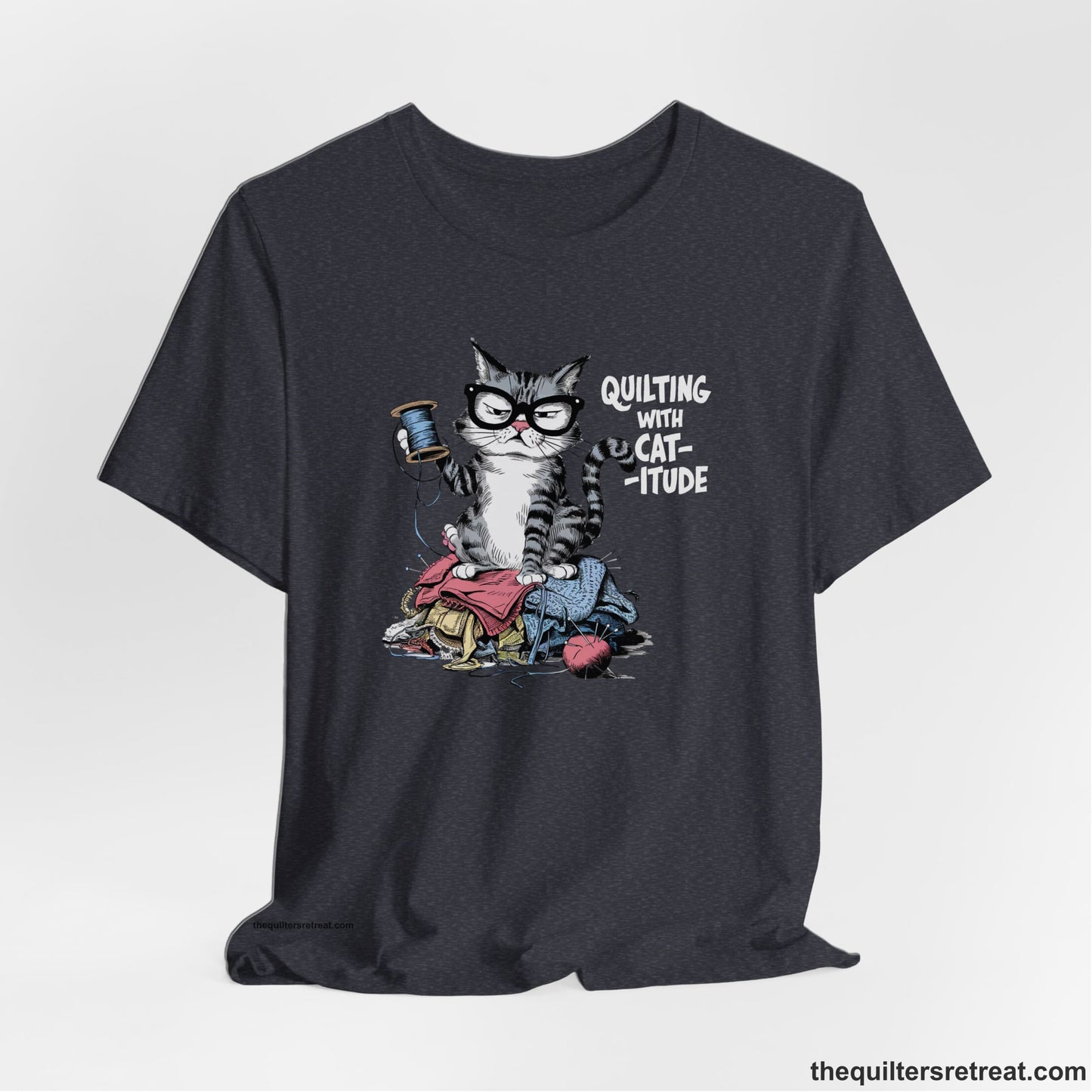 A Heather Navy Short Sleeve T-Shirt with a grumpy cat holding thread spool atop fabric pile with "Quilting with Cat-itude" text