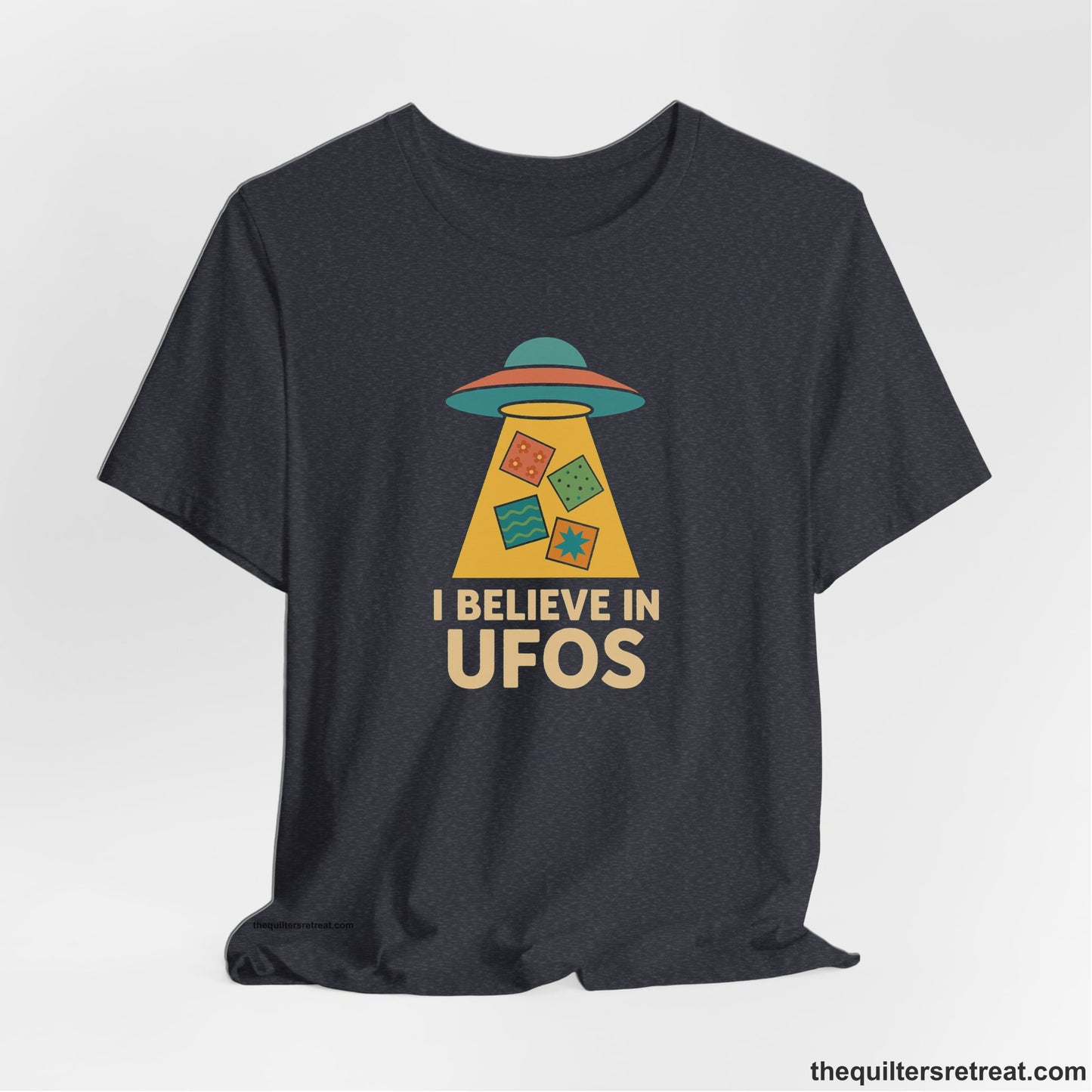 A Heather Navy Short Sleeve T-Shirt with a colorful UFO with quilt patterns and bold "I Believe in UFOs" text in retro style