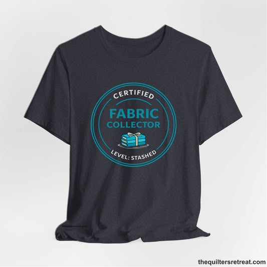 A Heather Navy Short Sleeve T-Shirt with a Circular teal logo with a whimsical fabric stack design, text "Fabric Collector".