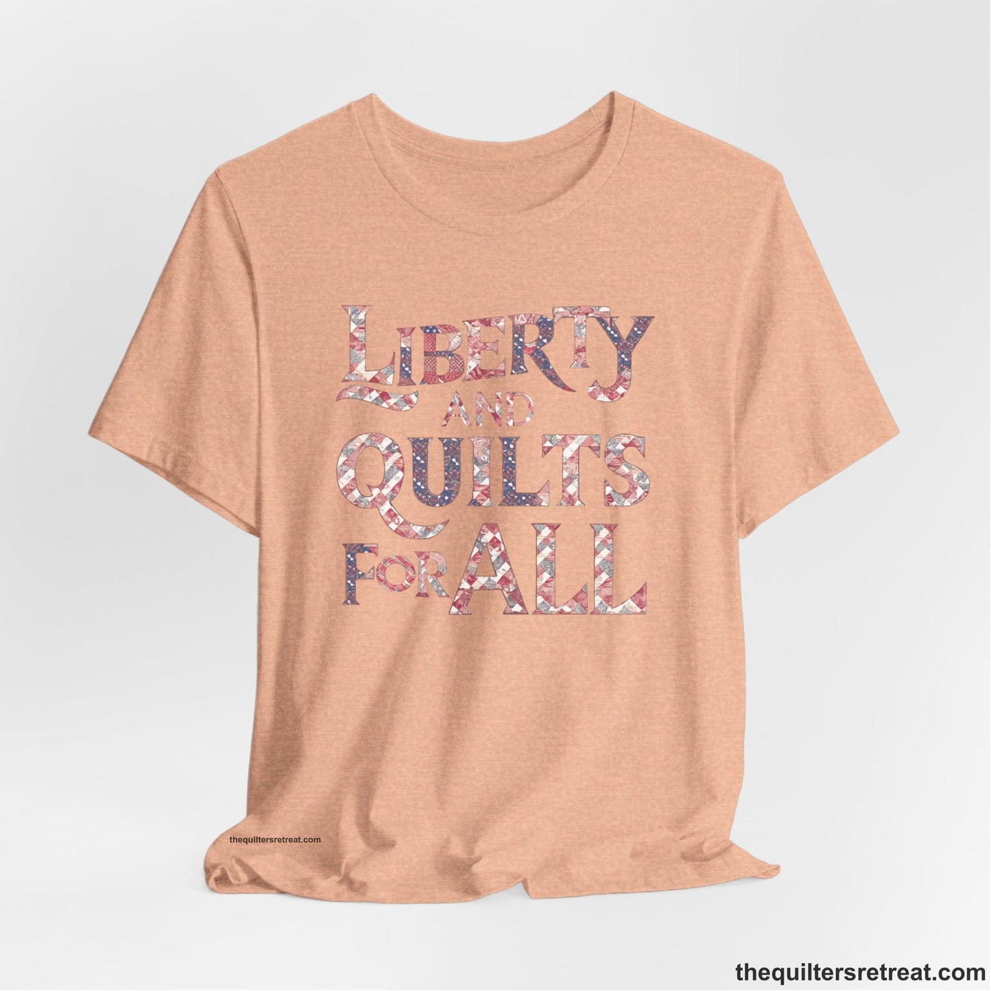 A Heather Peach Short Sleeve T-Shirt with a Liberty and Quilts for All" text with patchwork quilt pattern in a vintage style