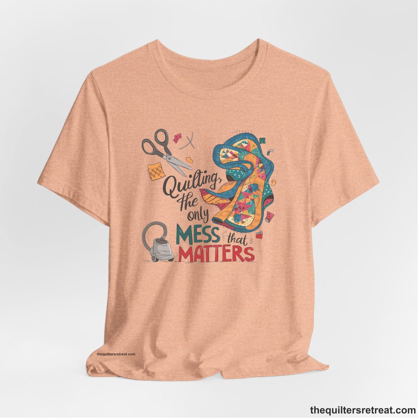 A Heather Peach Short Sleeve T-Shirt with a quilting tools and patchwork pieces with bold "Quilting, the only mess that matters" text