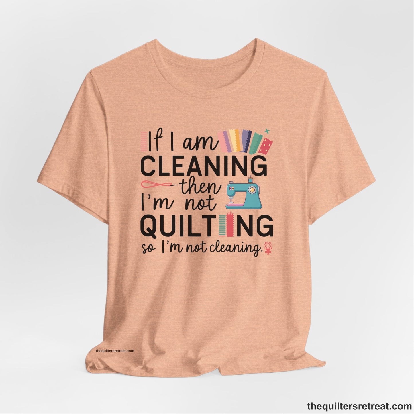 A Heather Peach Short Sleeve T-Shirt with a If I am cleaning then I'm not quilting text with sewing machine and fabric graphics