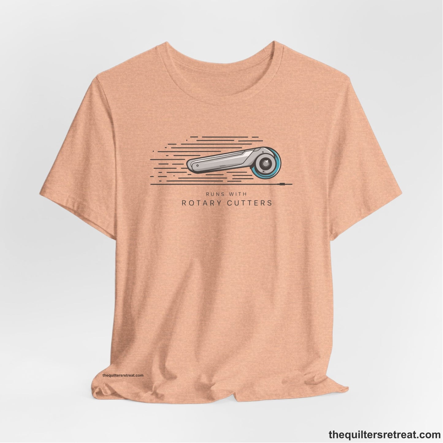 A Heather Peach Short Sleeve T-Shirt with a rotary cutter illustration with dynamic lines and bold "Runs with Rotary Cutters" text