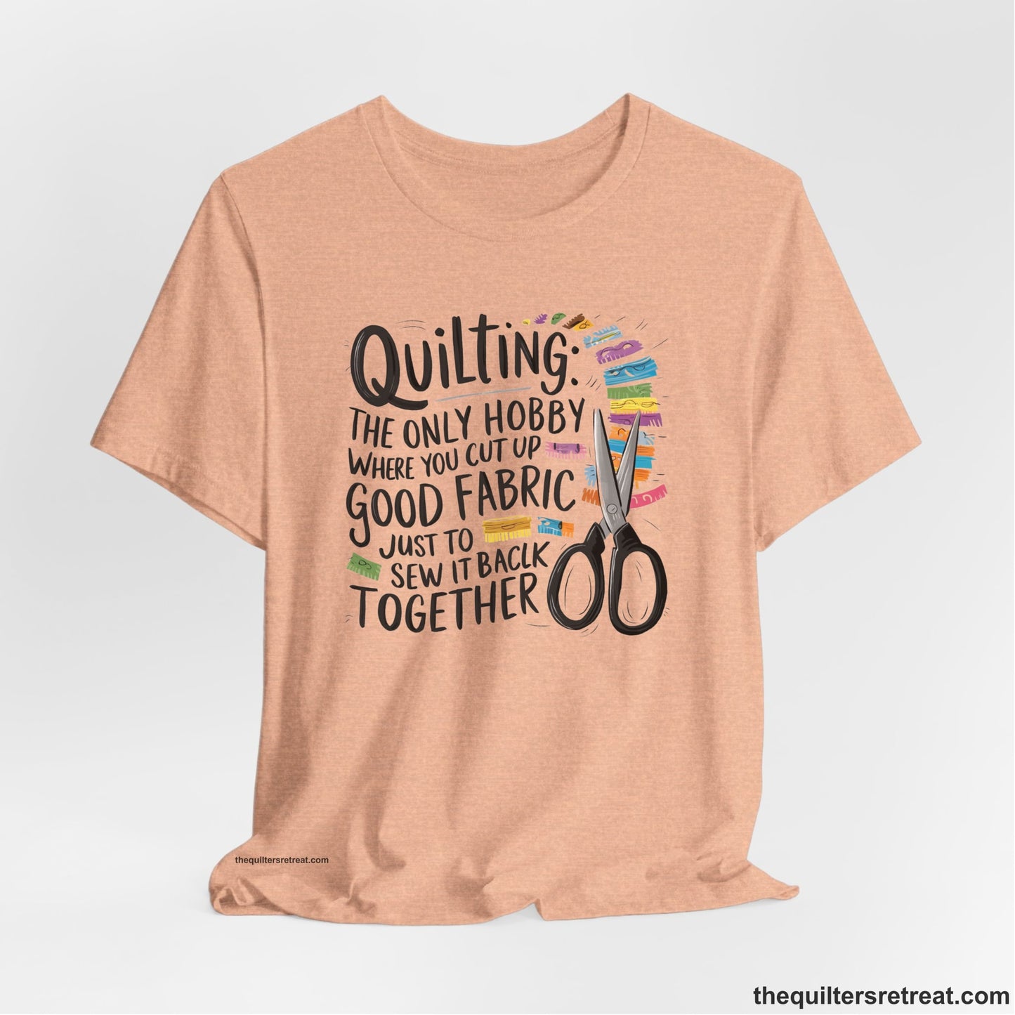 A Heather Peach Short Sleeve T-Shirt with a quilting-themed text with colorful fabric pieces and scissors in a whimsical style