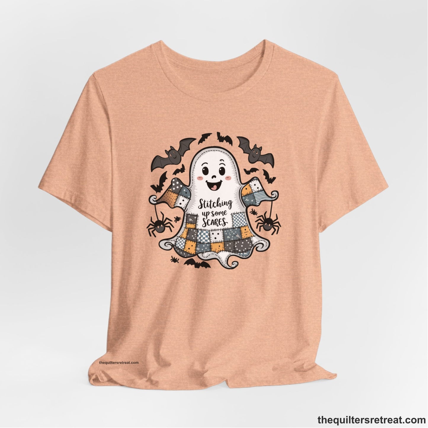 A Heather Peach Short Sleeve T-Shirt with a cute patchwork ghost with "Stitching up some Scares" text and playful bats in a whimsical style