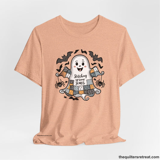 A Heather Peach Short Sleeve T-Shirt with a cute patchwork ghost with "Stitching up some Scares" text and playful bats in a whimsical style