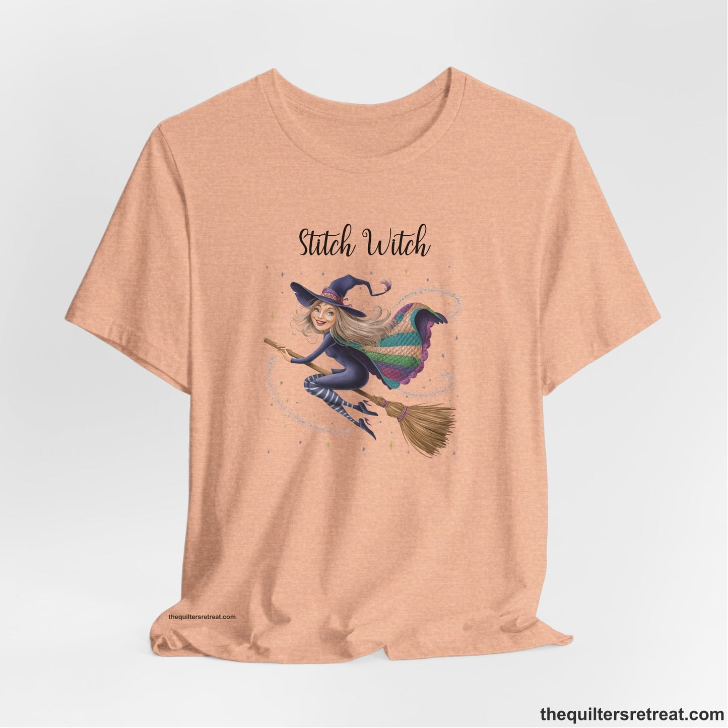 A Heather Peach Short Sleeve T-Shirt with a playful witch on broomstick with patchwork cape and starry background in a whimsical style