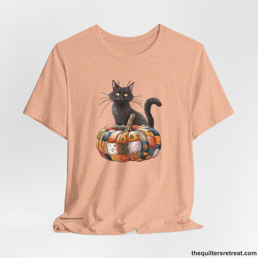 A Heather Peach Short Sleeve T-Shirt with a black cat with a quilted patchwork pumpkin in a whimsical autumn style