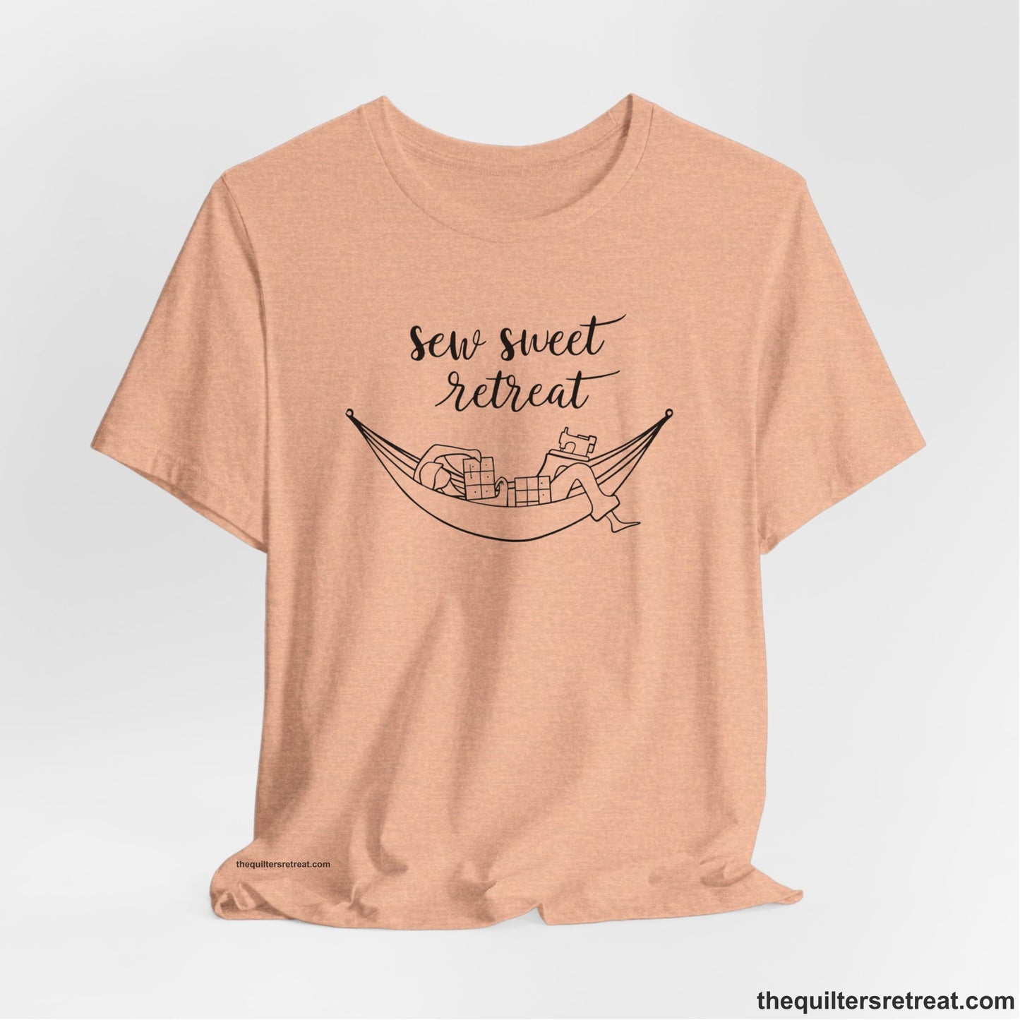 A Heather Peach Short Sleeve T-Shirt with a sewing machine and thread spools with "Sew Sweet Retreat" in whimsical script
