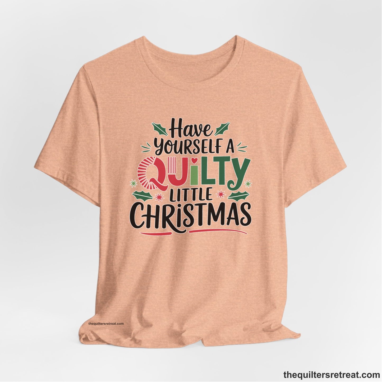 A Heather Peach Short Sleeve T-Shirt with a festive "Have Yourself a Quilty Little Christmas" text with holly and quilt patterns
