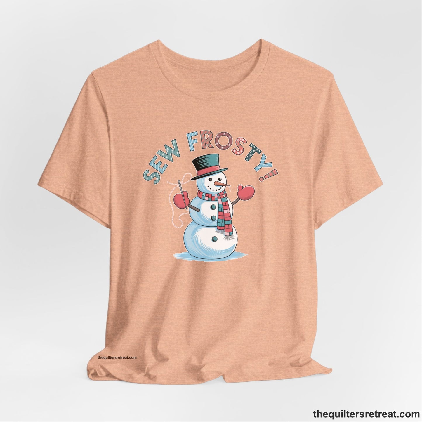 A Heather Peach Short Sleeve T-Shirt with a playful snowman sewing illustration with "Sew Frosty!" text in a festive style
