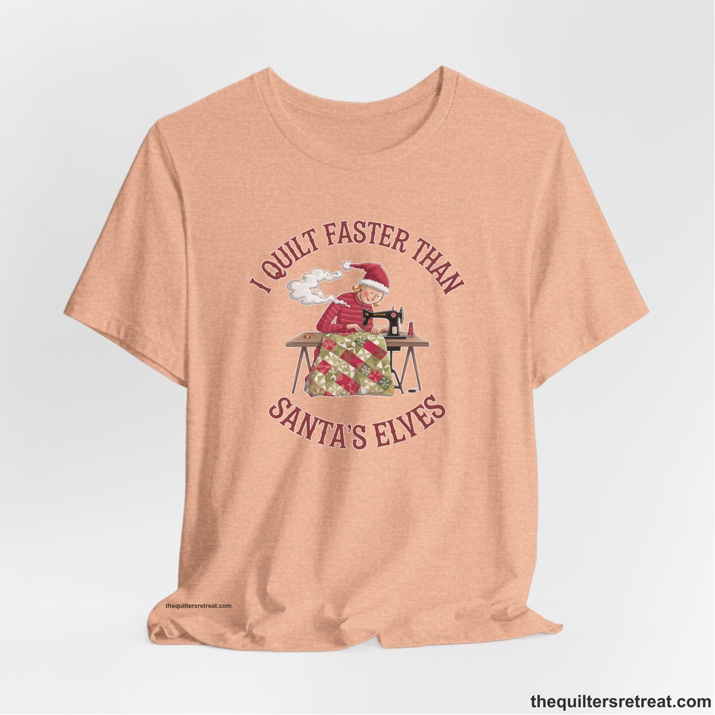 A Heather Peach Short Sleeve T-Shirt with a whimsical illustration of a quilting woman with "I Quilt Faster Than Santa's Elves" text