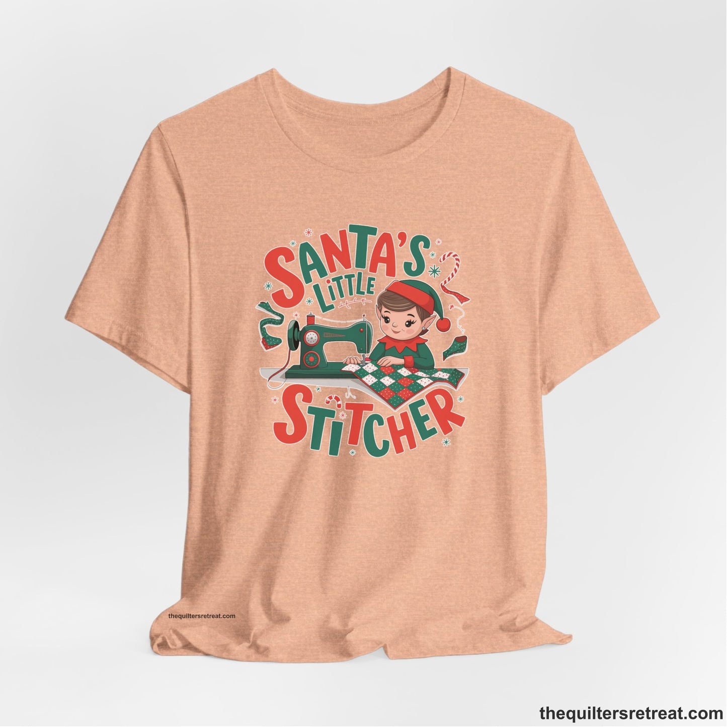 A Heather Peach Short Sleeve T-Shirt with a santa's little stitcher elf sewing quilt with festive colors in playful style