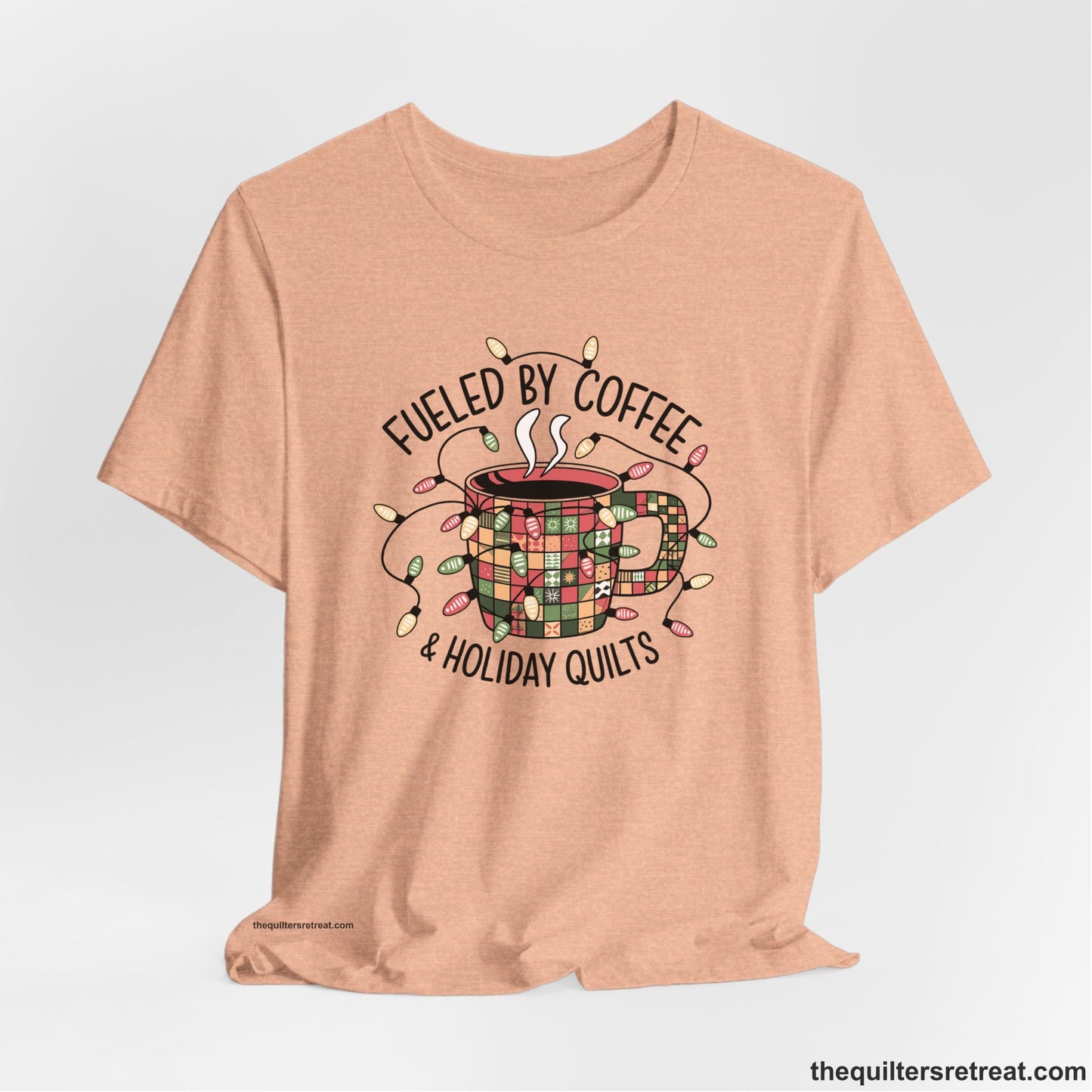 A Heather Peach Short Sleeve T-Shirt with a patchwork coffee mug with colorful lights and subtle "Fueled by Coffee" text in festive style