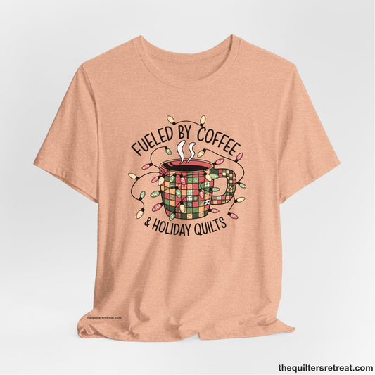 A Heather Peach Short Sleeve T-Shirt with a patchwork coffee mug with colorful lights and subtle "Fueled by Coffee" text in festive style