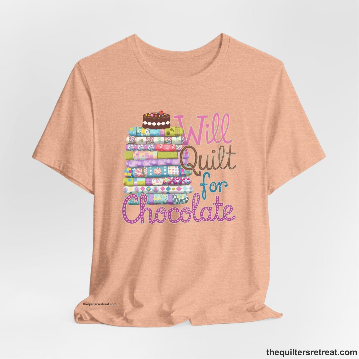 A Heather Peach Short Sleeve T-Shirt with a stack of colorful quilts topped with cake, whimsical "Will Quilt for Chocolate" text