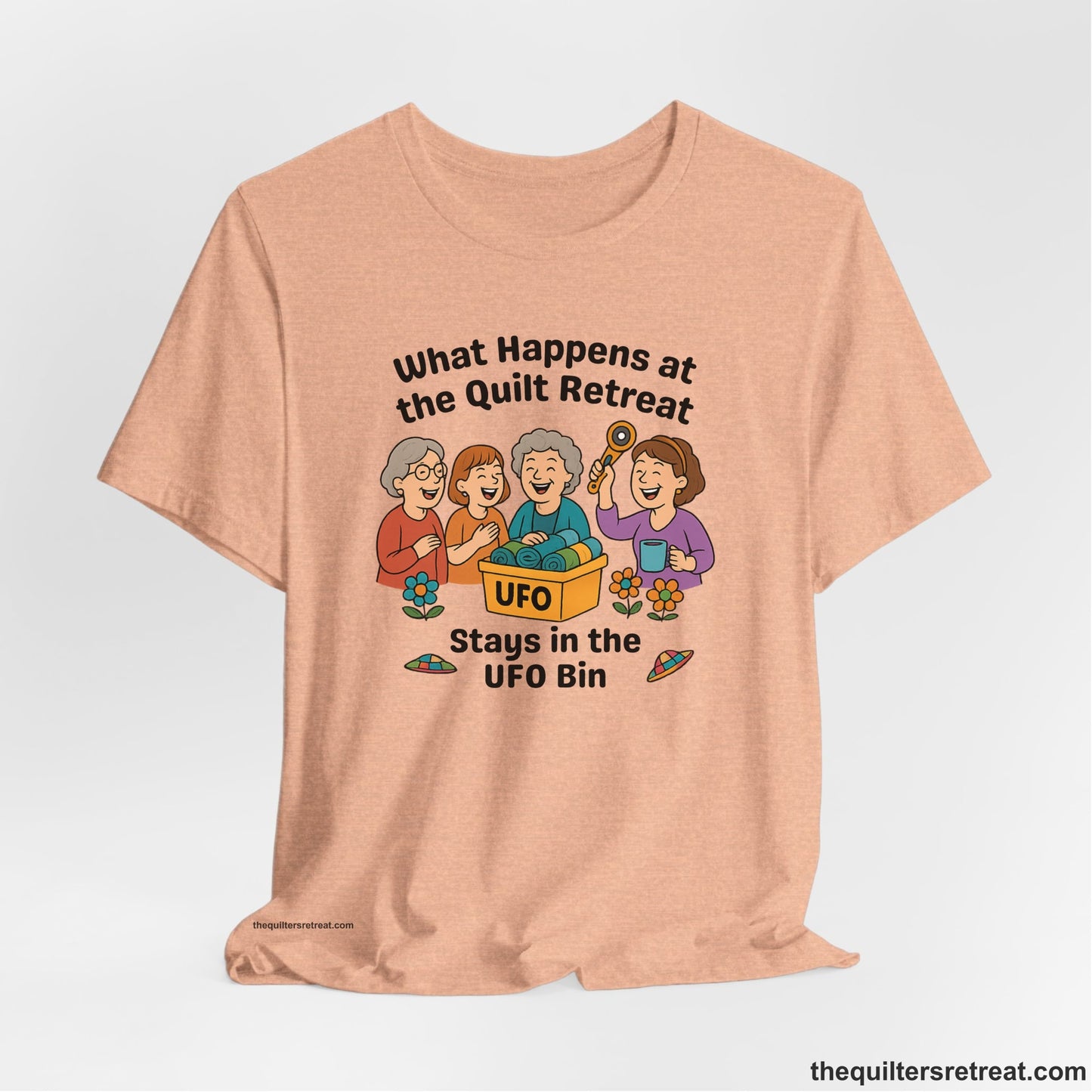A Heather Peach Short Sleeve T-Shirt with a four smiling women with unfinished fabric objects and playful "UFO" text in a cartoon style