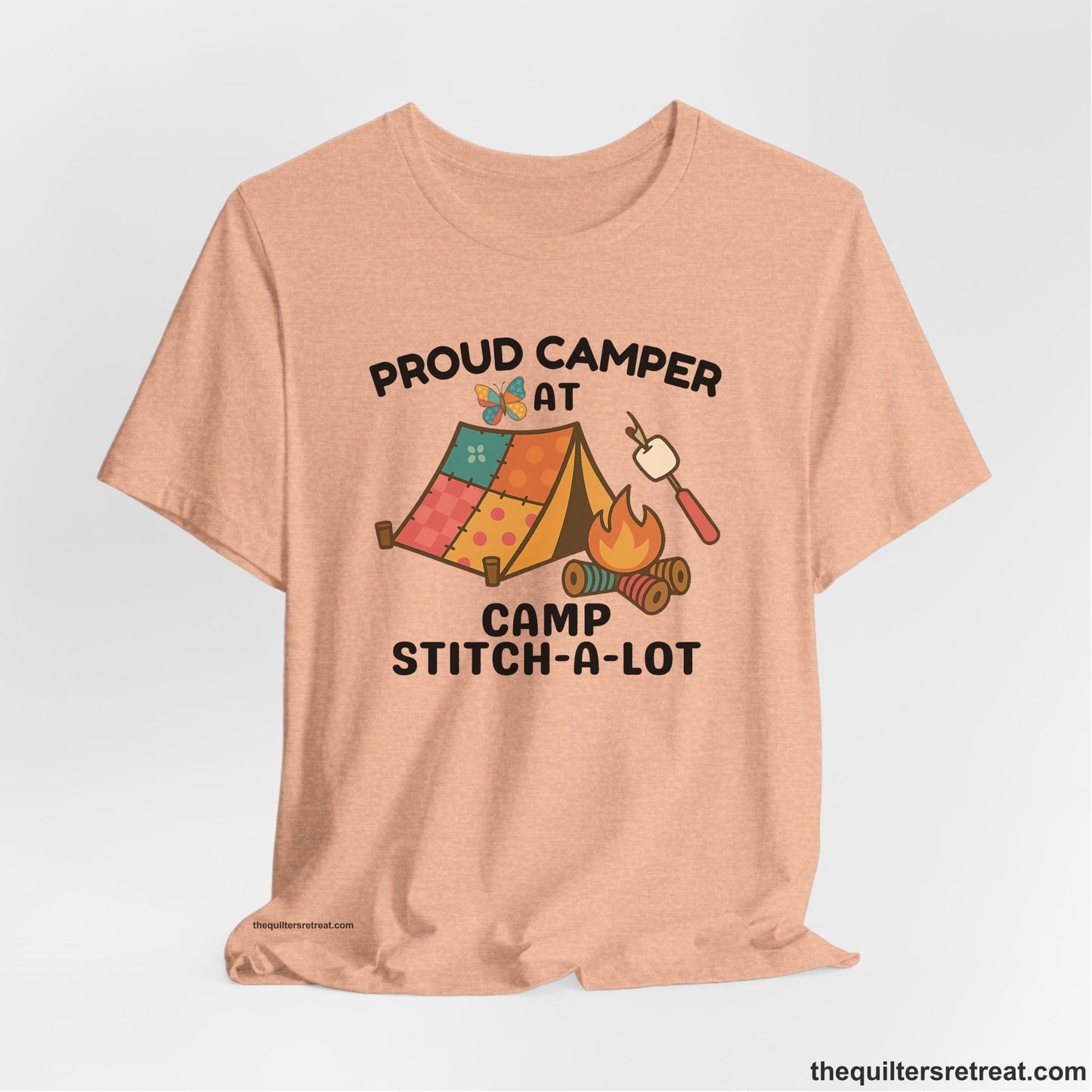 A Heather Peach Short Sleeve T-Shirt with a camping scene with patchwork tent, campfire, and whimsical butterfly and marshmallow illustration