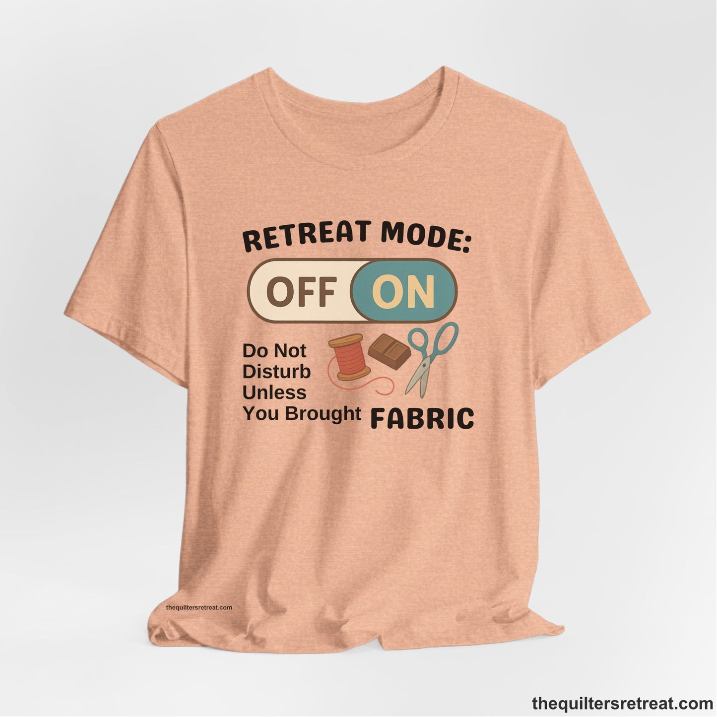 A Heather Peach Short Sleeve T-Shirt with a illustration of sewing tools with a playful "OFF ON" switch design