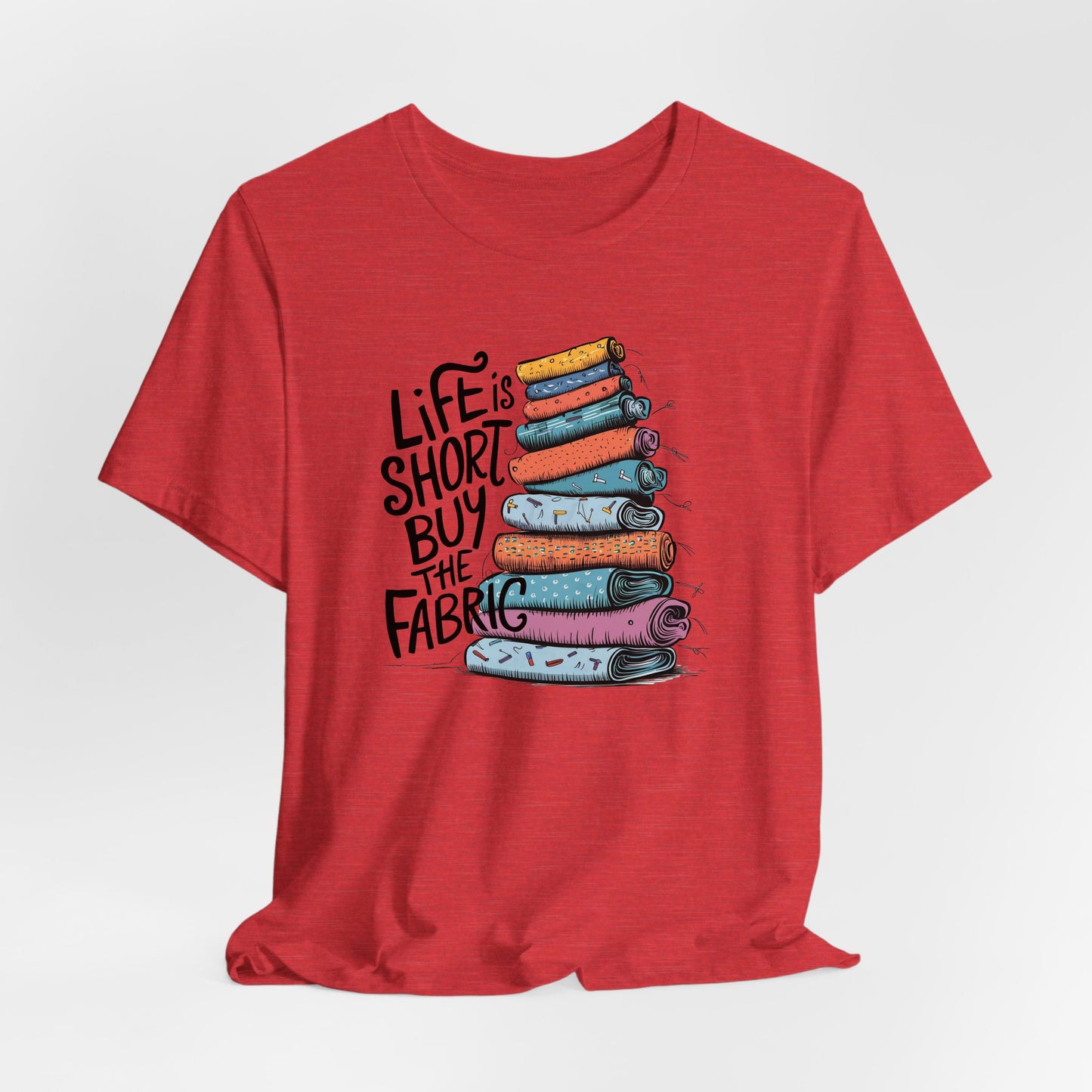A Heather Red Short Sleeve T-Shirt with a illustration of colorful fabric rolls with bold "Life is Short Buy the Fabric" text