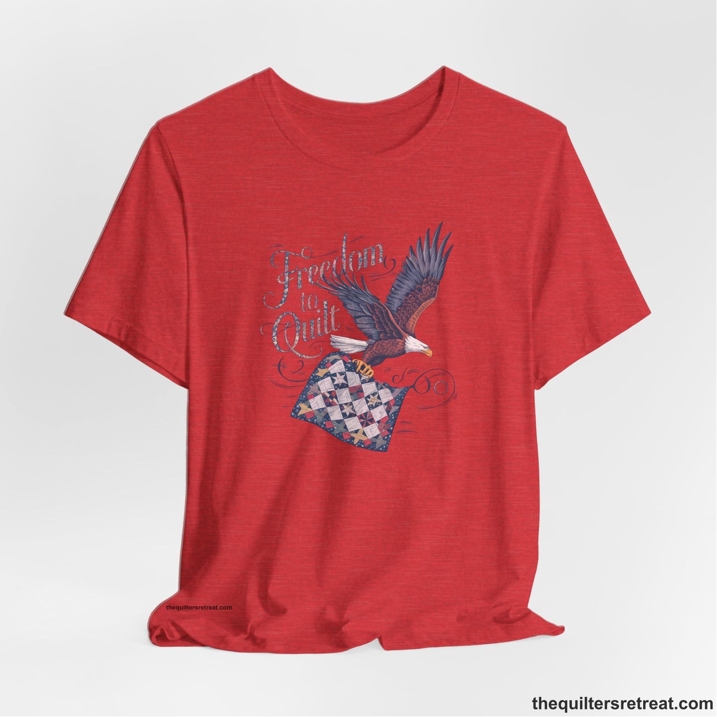 A Heather Red Short Sleeve T-Shirt with a freedom to quilt text with an eagle carrying a colorful patchwork quilt in vintage style