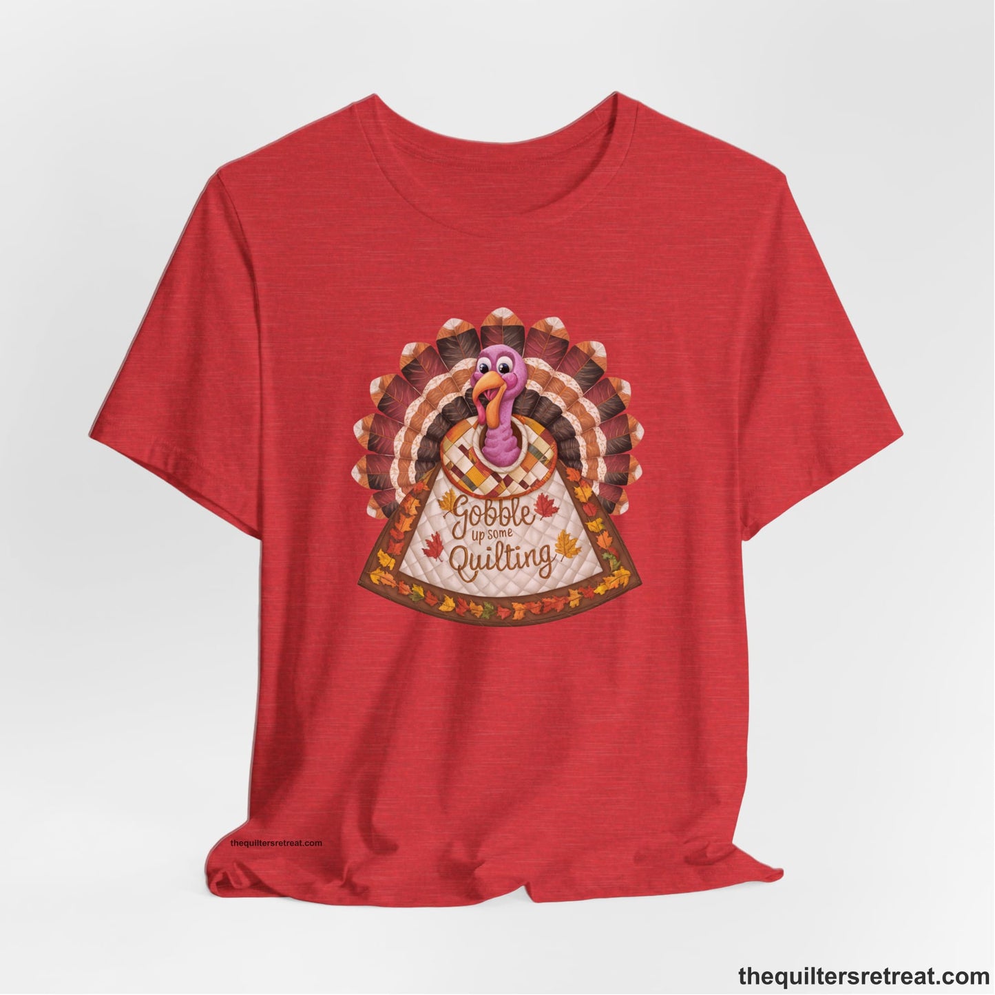 A Heather Red Short Sleeve T-Shirt with a colorful turkey with quilted feathers and "Gobble Up Some Quilting" text in a playful style