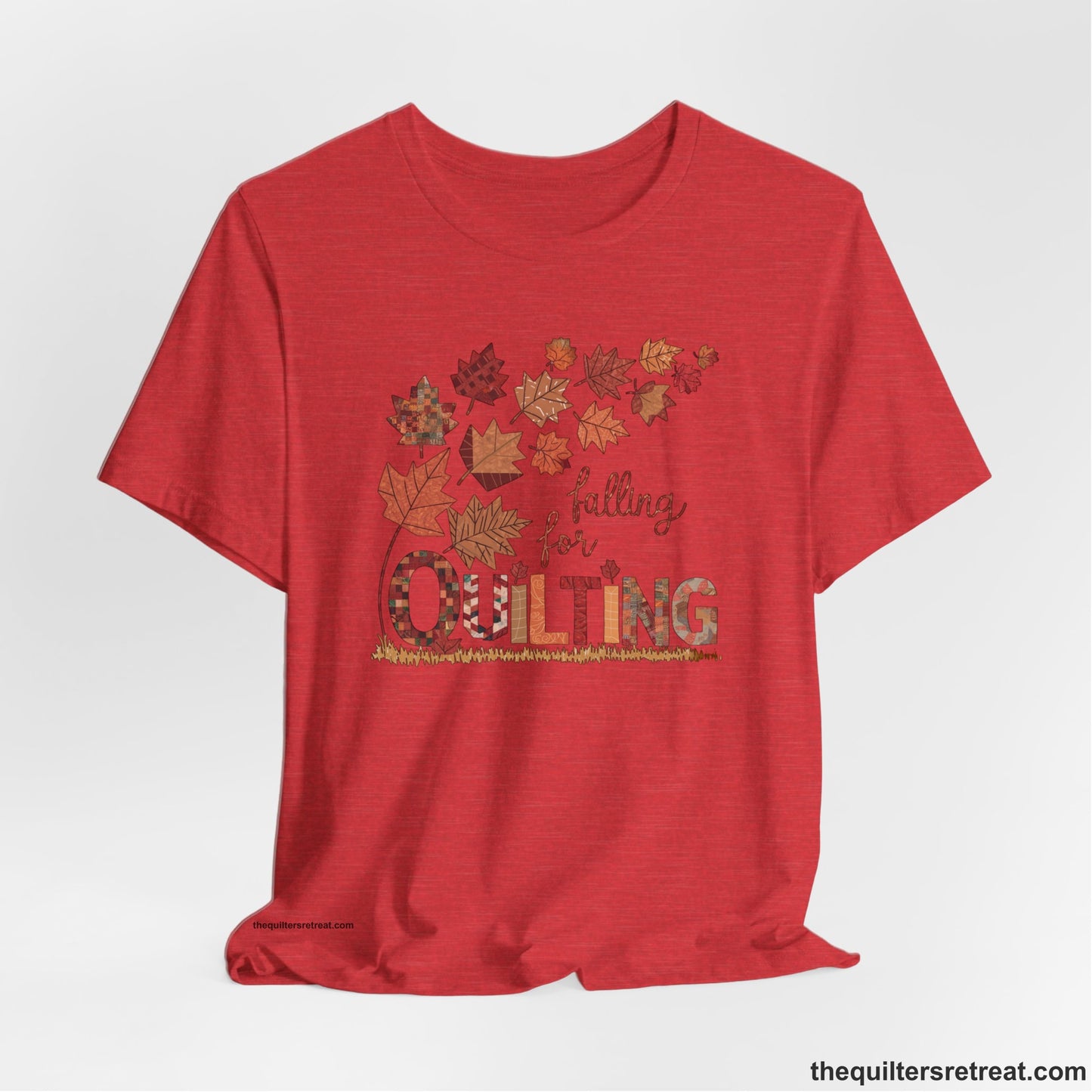 A Heather Red Short Sleeve T-Shirt with a falling autumn leaves and "Falling for Quilting" text in a patchwork style