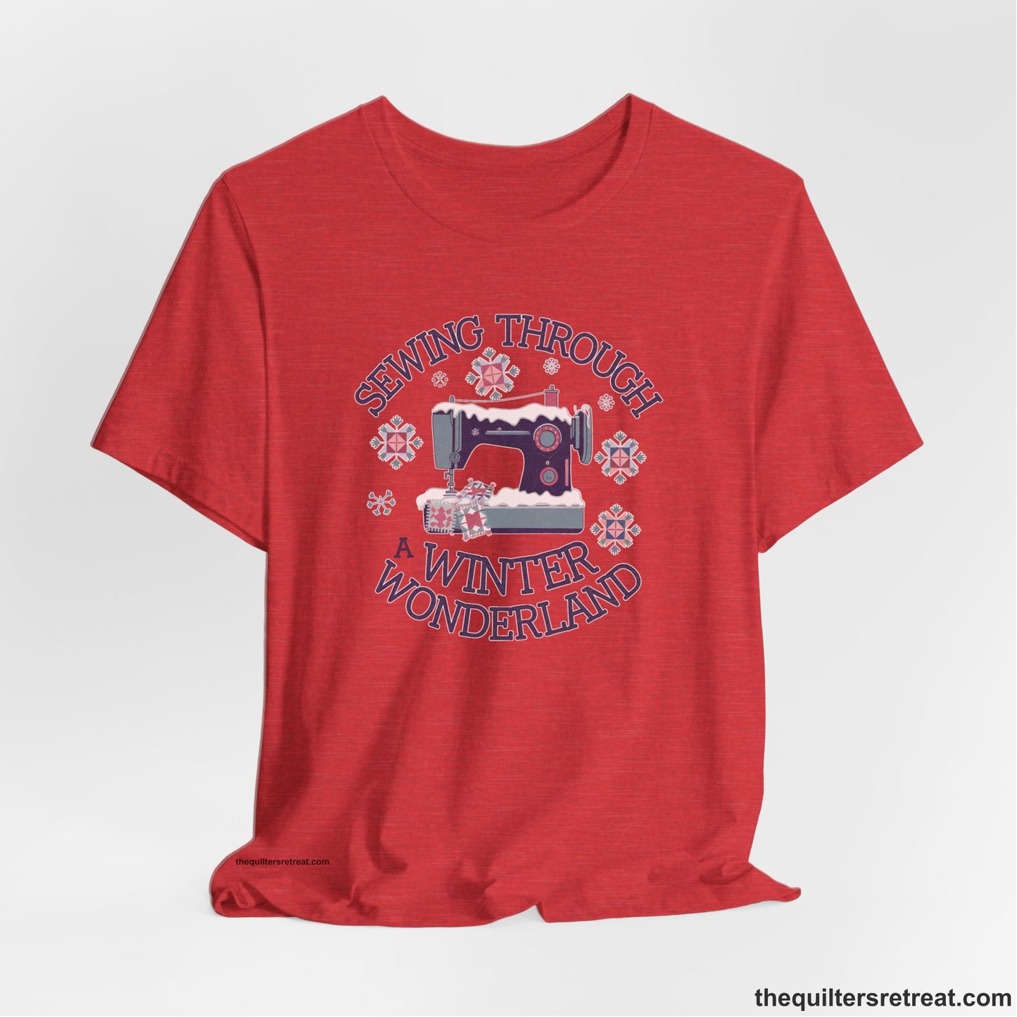 A Heather Red Short Sleeve T-Shirt with a sewing machine covered in snow with festive quilting elements and "Sewing Through a Winter Wonderland" text