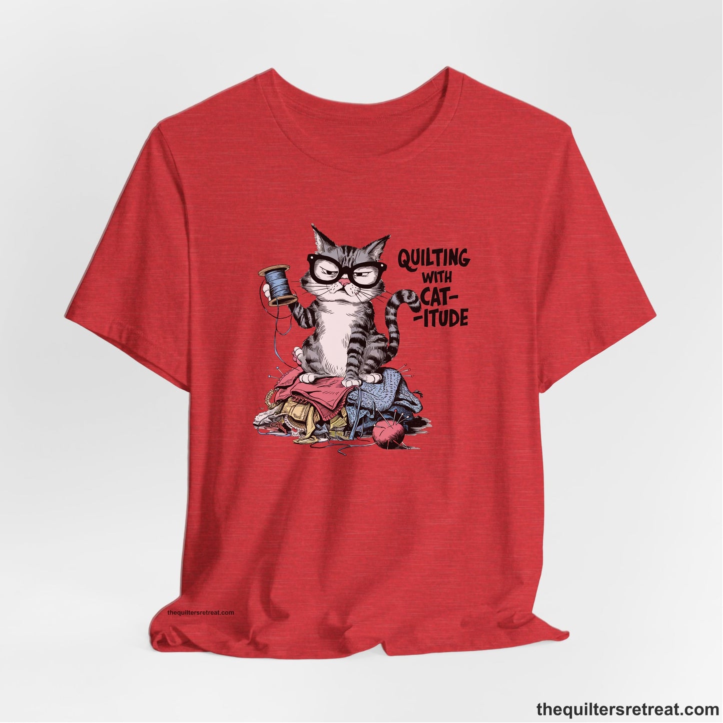 A Heather Red Short Sleeve T-Shirt with a grumpy cat holding thread spool atop fabric pile with "Quilting with Cat-itude" text