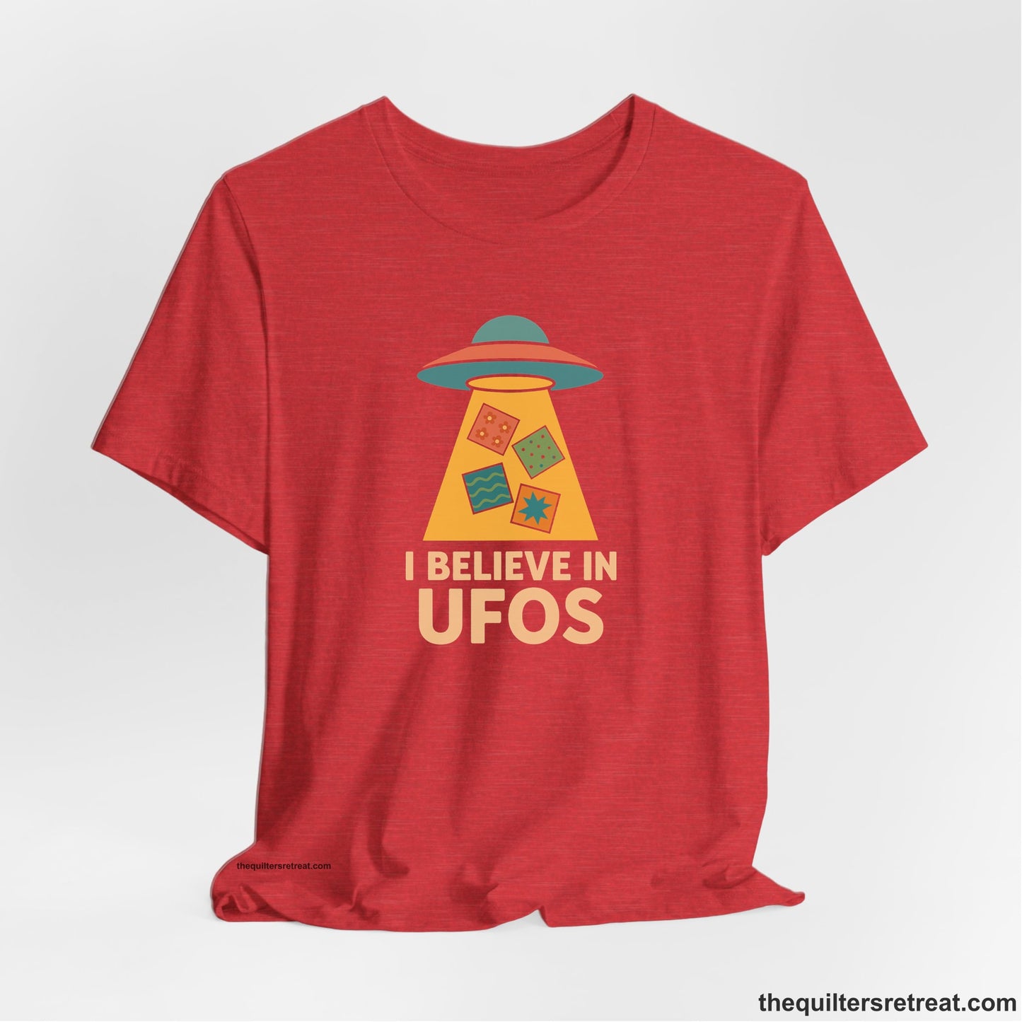 A Heather Red Short Sleeve T-Shirt with a colorful UFO with quilt patterns and bold "I Believe in UFOs" text in retro style