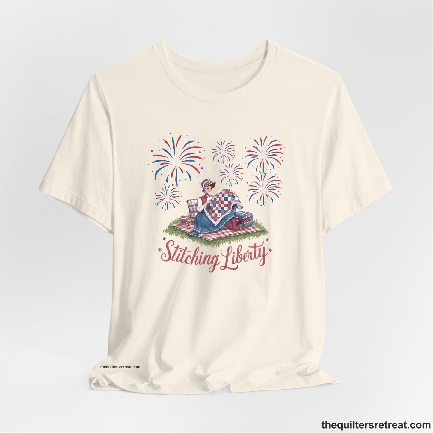 A Natural Short Sleeve T-Shirt with a vintage illustration of woman quilting with fireworks and "Stitching Liberty" text in patriotic style
