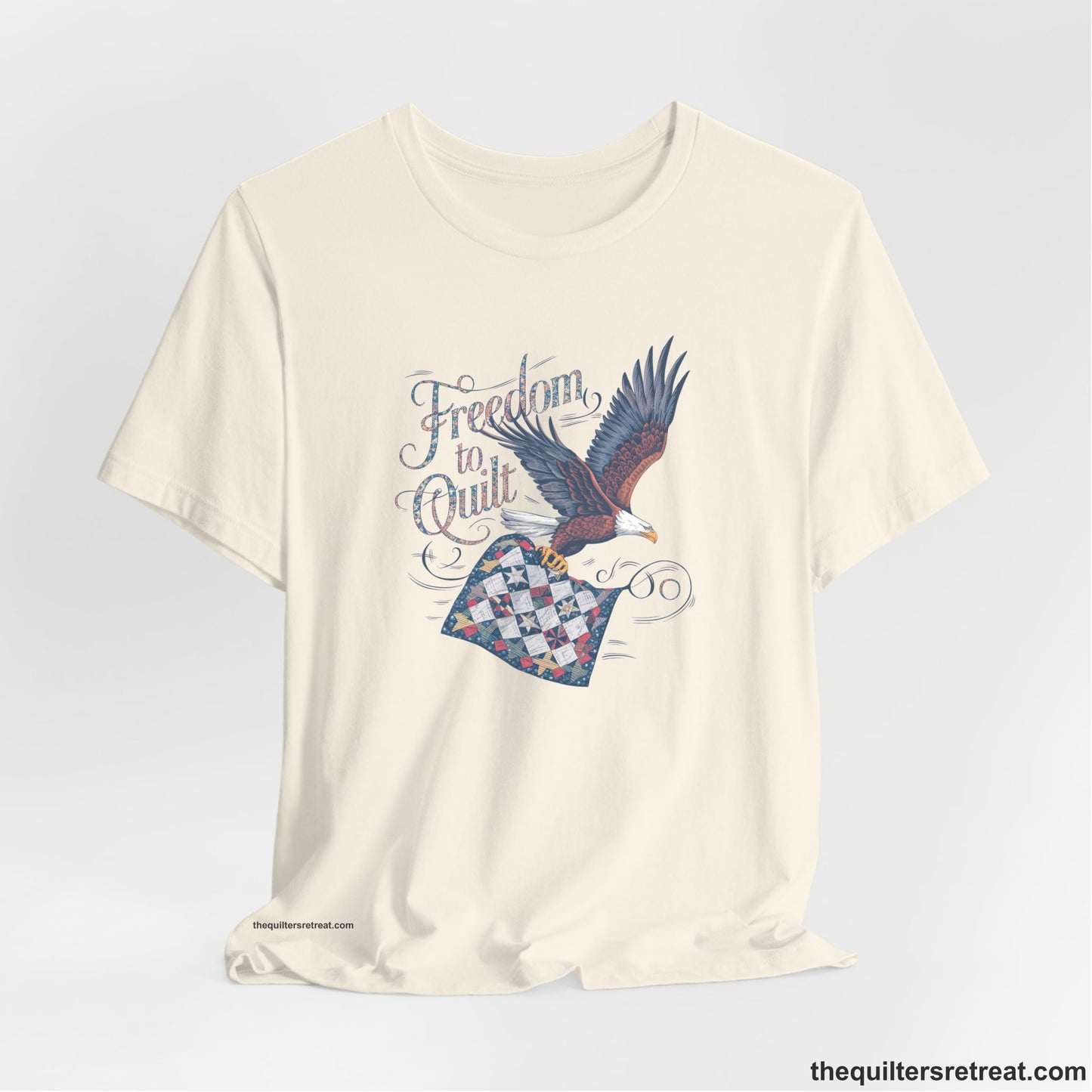 A Natural Short Sleeve T-Shirt with a freedom to quilt text with an eagle carrying a colorful patchwork quilt in vintage style