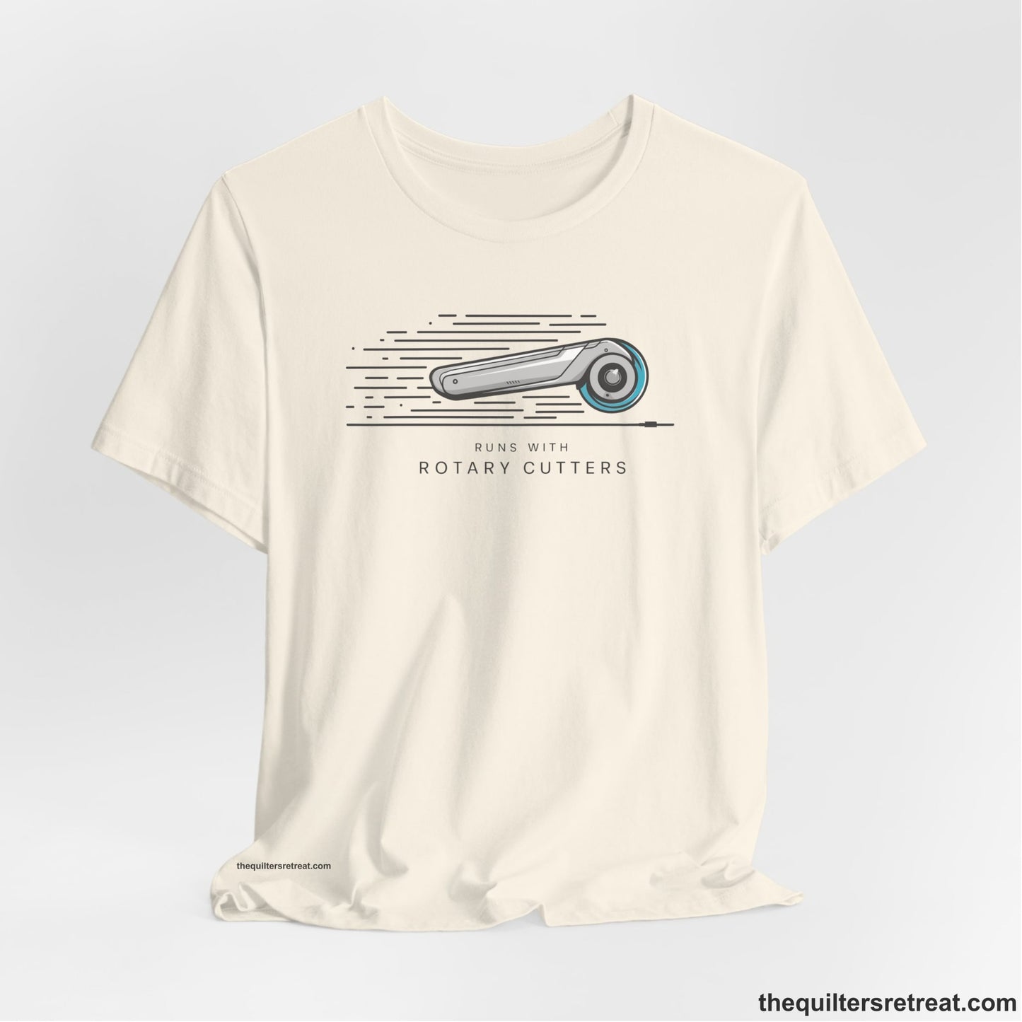 A Natural Short Sleeve T-Shirt with a rotary cutter illustration with dynamic lines and bold "Runs with Rotary Cutters" text