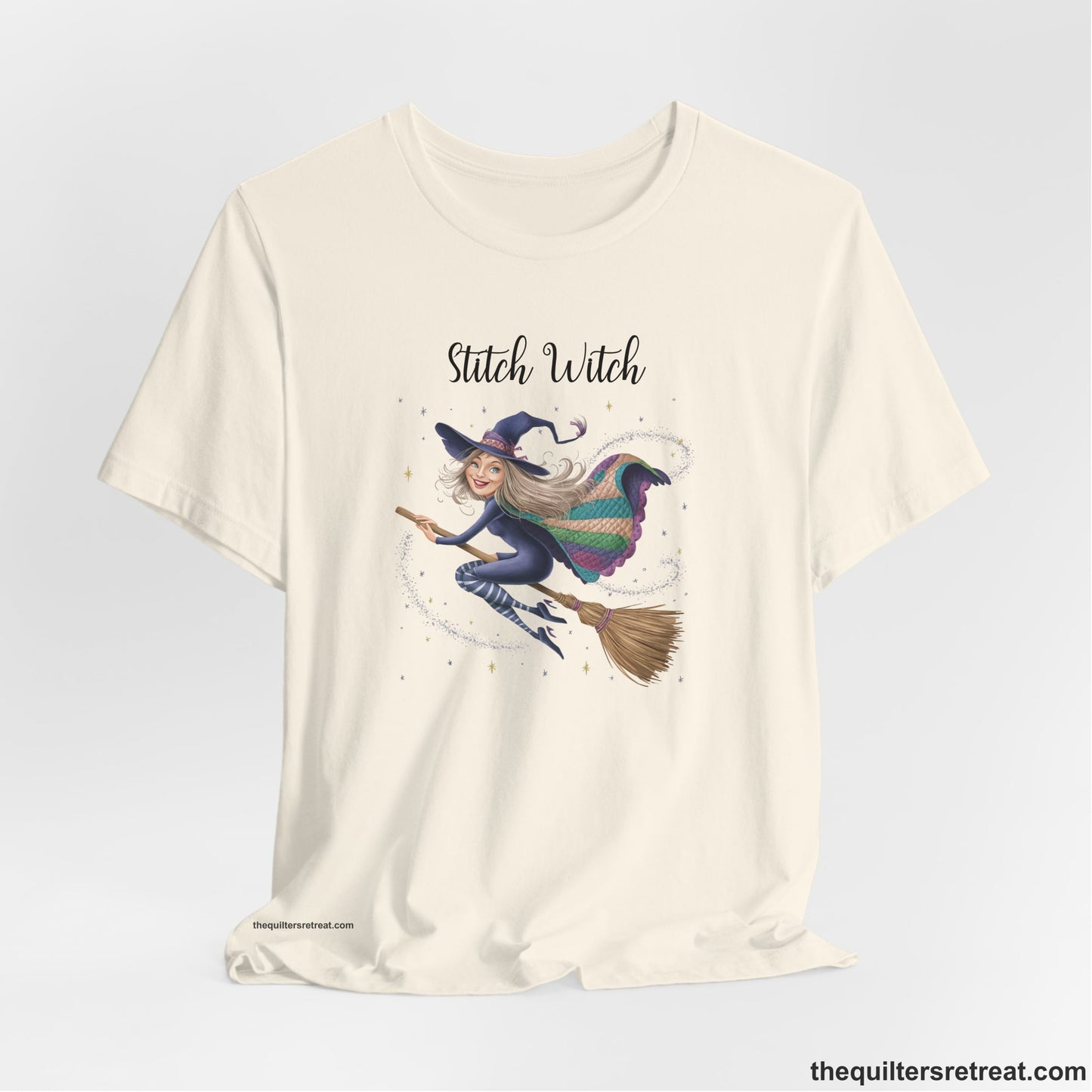 A Natural Short Sleeve T-Shirt with a playful witch on broomstick with patchwork cape and starry background in a whimsical style