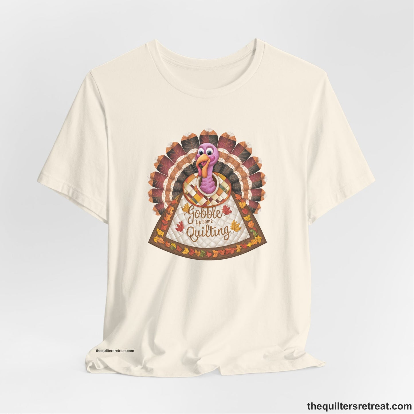 A Natural Short Sleeve T-Shirt with a colorful turkey with quilted feathers and "Gobble Up Some Quilting" text in a playful style