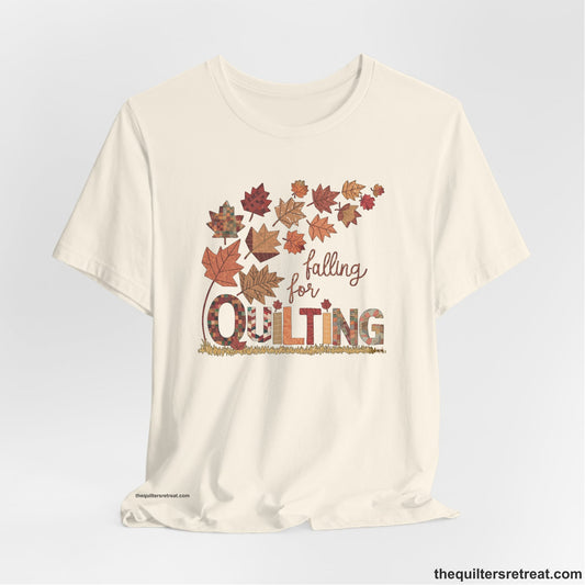 A Natural Short Sleeve T-Shirt with a falling autumn leaves and "Falling for Quilting" text in a patchwork style