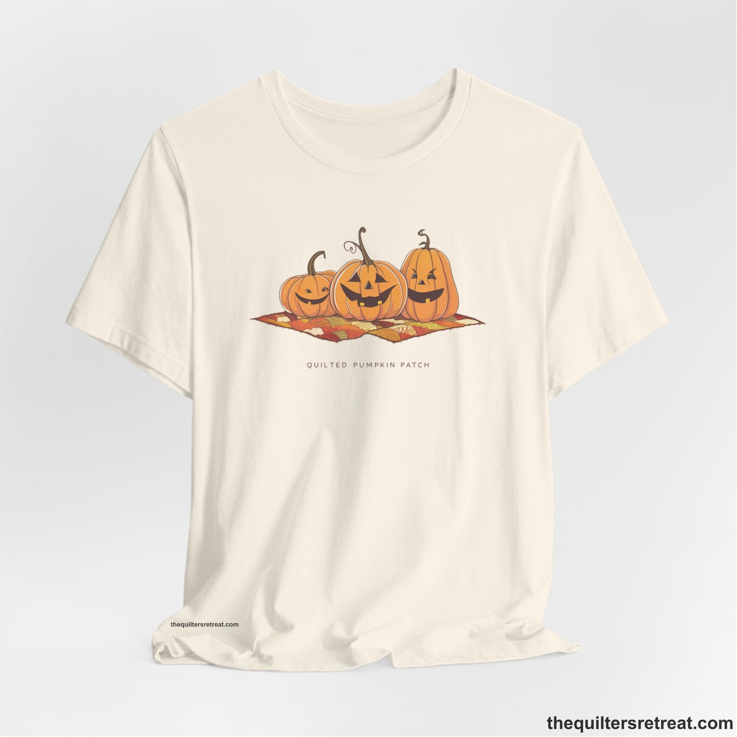 A Natural Short Sleeve T-Shirt with a playful jack-o'-lantern trio on a quilt with "Quilted Pumpkin Patch" text