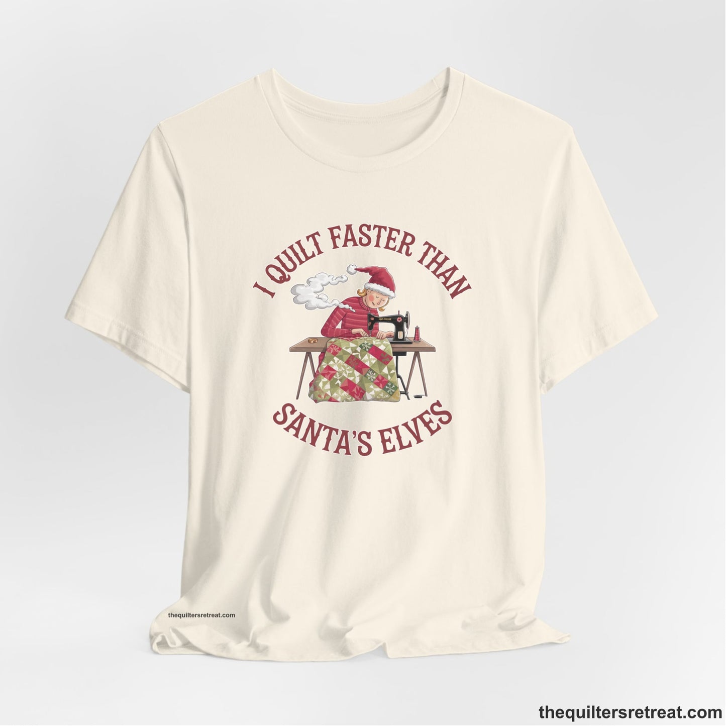 A Natural Short Sleeve T-Shirt with a whimsical illustration of a quilting woman with "I Quilt Faster Than Santa's Elves" text