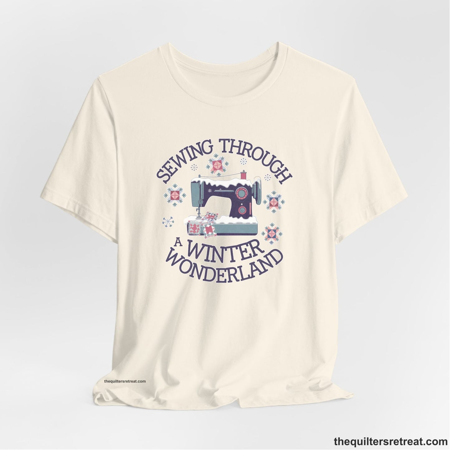 A Natural Short Sleeve T-Shirt with a sewing machine covered in snow with festive quilting elements and "Sewing Through a Winter Wonderland" text
