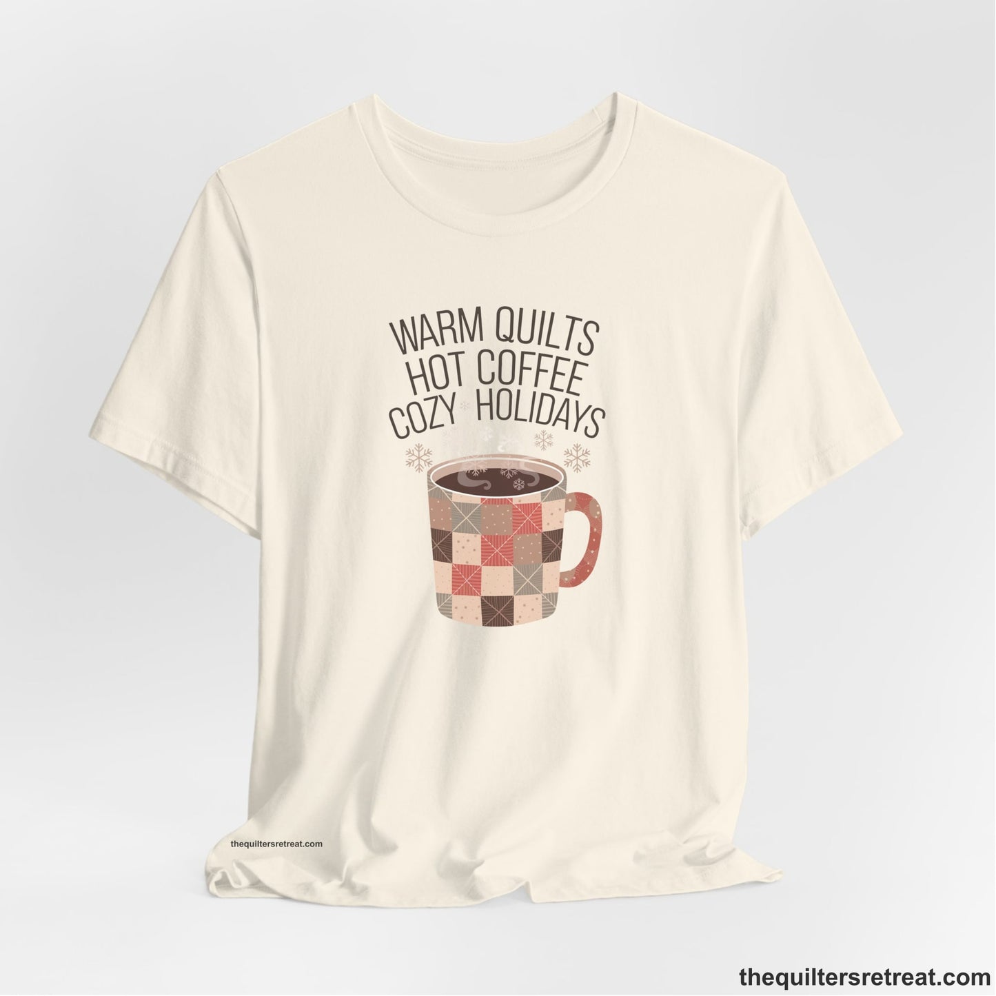 A Natural Short Sleeve T-Shirt with a warm quilts hot coffee cozy holidays text with a patchwork mug and snowflakes