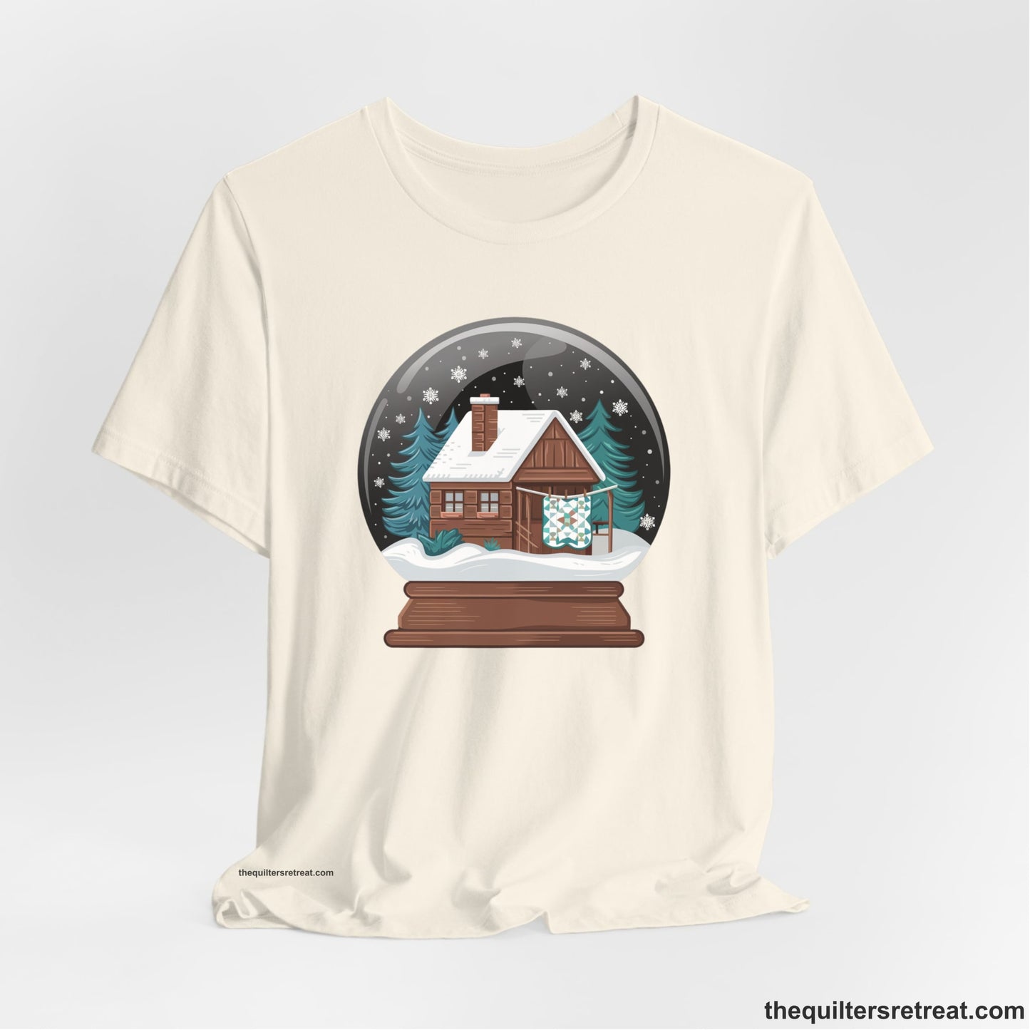 A Natural Short Sleeve T-Shirt with a cabin in a snow globe with snowflakes and trees, in a cozy rustic style
