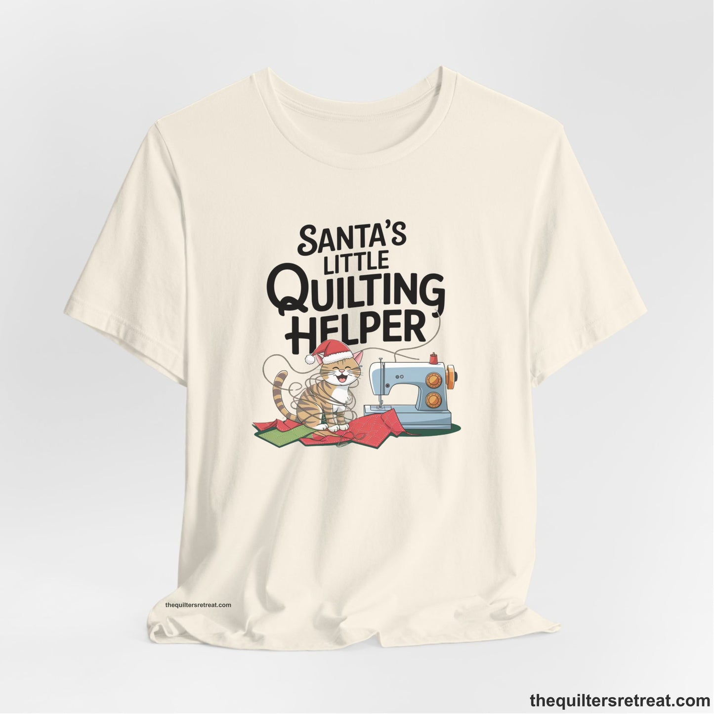 A Natural Short Sleeve T-Shirt with a santa-hat-wearing kitten with a sewing machine and "Santa's Little Quilting Helper" text in playful style