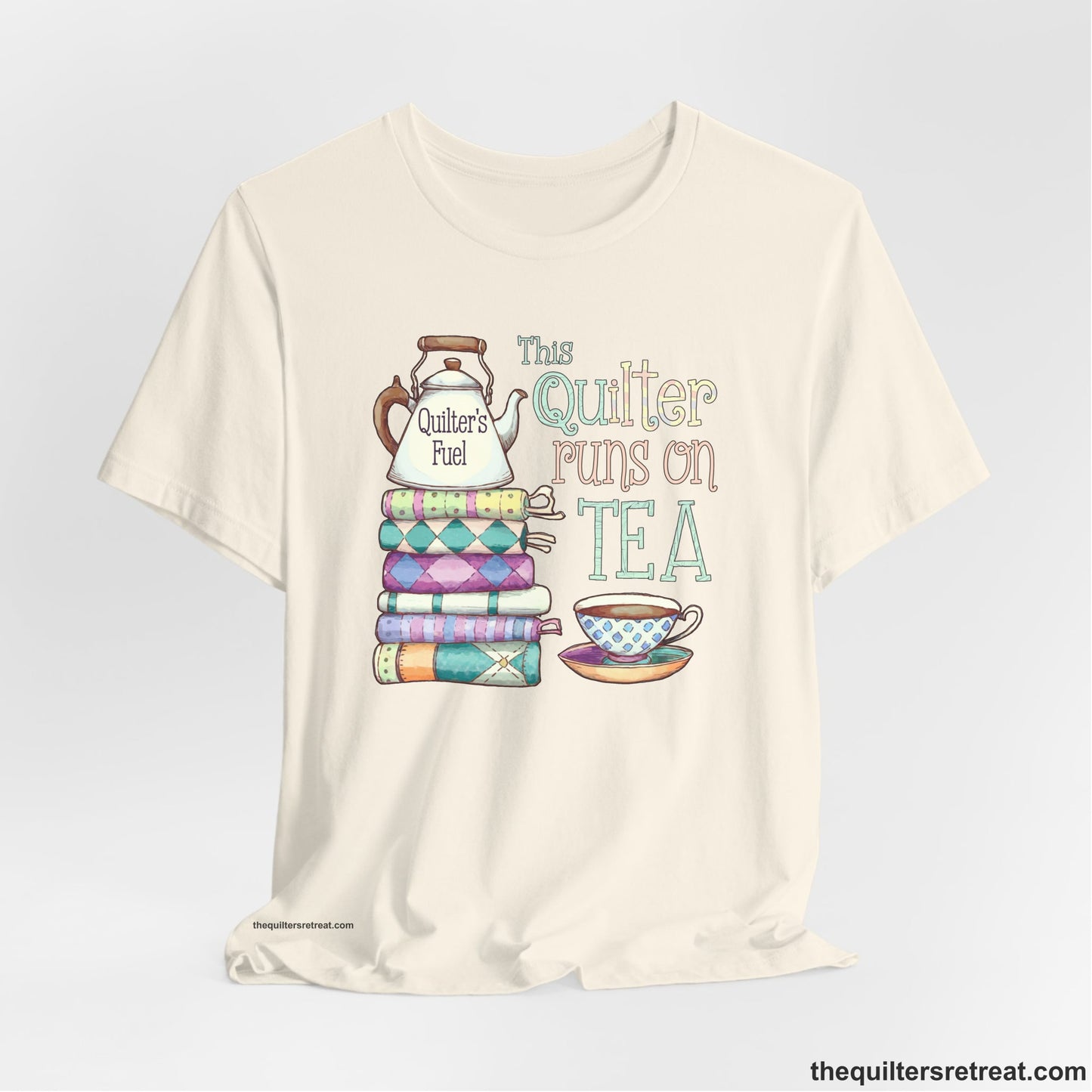 A Natural Short Sleeve T-Shirt with a stack of colorful quilts with teapot and cup, whimsical "This Quilter Runs on Tea" text